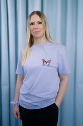 T-Shirt aus 100 % Bio-Baumwolle mit normaler Passform, erhältlich in verschiedenen Farben wie Blue Soul, Cotton Pink, Lavender, Aloe, Weiss und Schwarz. Individuell bedruckbar mit Wunschmotiv. Weiches, angenehm leichtes Material für hohen Tragekomfort. Ideal für einen zeitgemässen, entspannten Look. Vorderseite: Farbiger Schmetterling auf der linken Brust. Rückseite: Buntes Blumen- und Schmetterlingsfeld im Illustrationsstil.