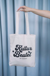 Naturfarbene Tote Bag mit schwarzem oder rosa Retro-Schriftzug „Kultur Beutel BY ANWAY“, grosse Stofftasche aus 80% recycelter Baumwolle und 20% recyceltem Polyester, mit langen Henkeln und robustem Schnitt – ideal als stylischer Alltagsbegleiter.