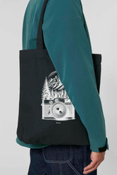 Schwarze Tote Bag mit weissem Vintage-Motiv einer analogen, alten Kamera vor einem Bergpanorama und Tannen – hochwertige Stofftasche aus 80% recycelter Baumwolle und 20% recyceltem Polyester, ideal für Natur- und Fotografie-Liebhaber.
