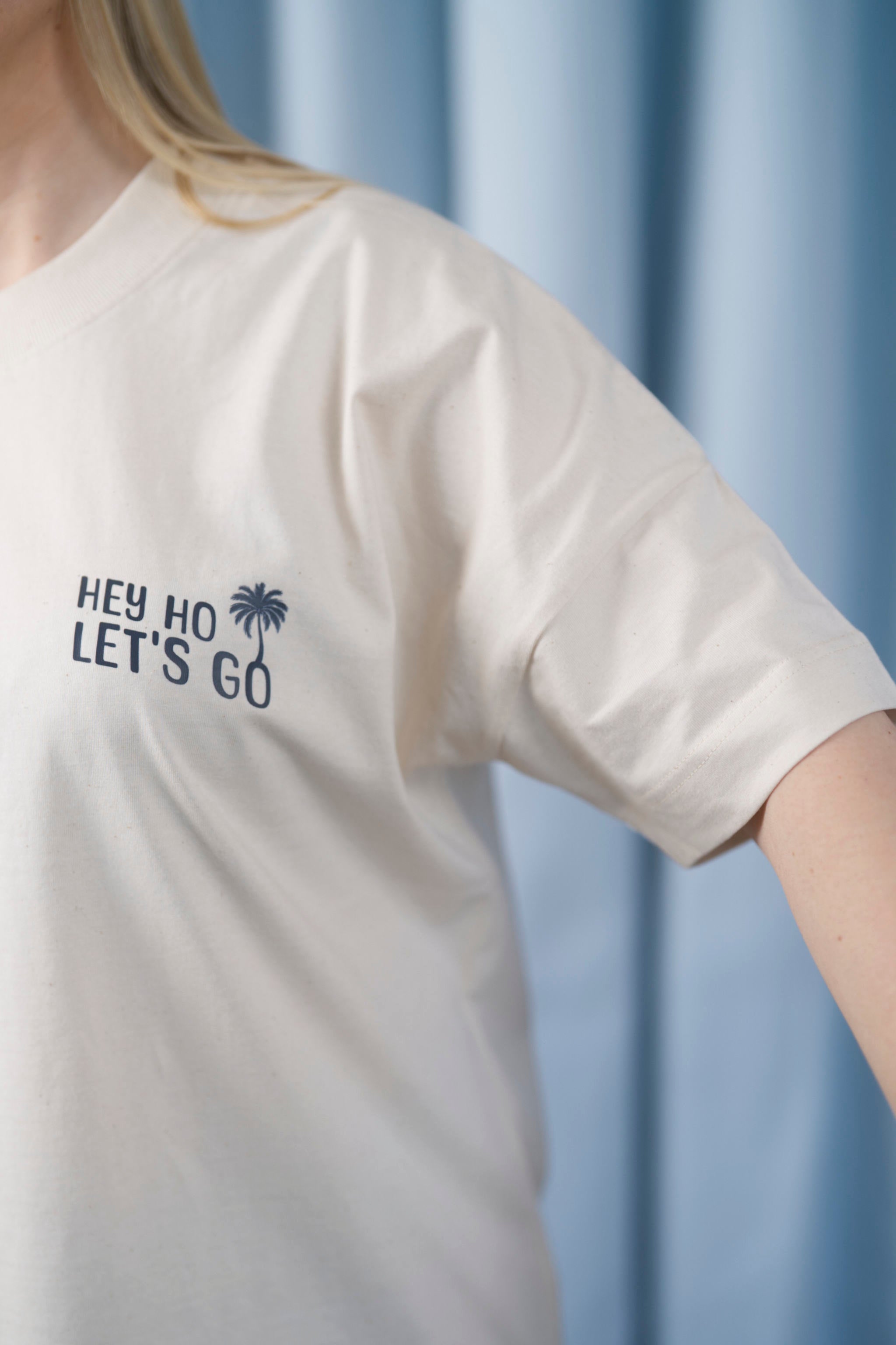 Oversized T-Shirt aus 100 % Bio-Baumwolle mit weitem, modernem Schnitt, erhältlich in Schwarz, Weiss und Natur. Individuell gestaltbar mit Wunschmotiv und frei wählbarer Platzierung. Weiche Qualität, überschnittene Ärmelansätze und lässiger Style für maximalen Tragekomfort. Mit Retro-Bus-Print, Palmen und „HEY HO LET'S GO“-Schriftzug.
