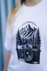 Oversized T-Shirt aus 100 % Bio-Baumwolle mit weitem, modernem Schnitt, erhältlich in Schwarz, Weiss und Natur. Individuell gestaltbar mit Wunschmotiv und frei wählbarer Platzierung. Weiche Qualität, überschnittene Ärmelansätze und lässiger Style für maximalen Tragekomfort. Mit retro Kamera-Illustration, Bergpanorama und Tannenwäldern auf der Brust.
