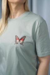 T-Shirt aus 100 % Bio-Baumwolle mit normaler Passform, erhältlich in verschiedenen Farben wie Blue Soul, Cotton Pink, Lavender, Aloe, Weiss und Schwarz. Individuell bedruckbar mit Wunschmotiv. Weiches, angenehm leichtes Material für hohen Tragekomfort. Ideal für einen zeitgemässen, entspannten Look. Vorderseite: Farbiger Schmetterling auf der linken Brust. Rückseite: Buntes Blumen- und Schmetterlingsfeld im Illustrationsstil.