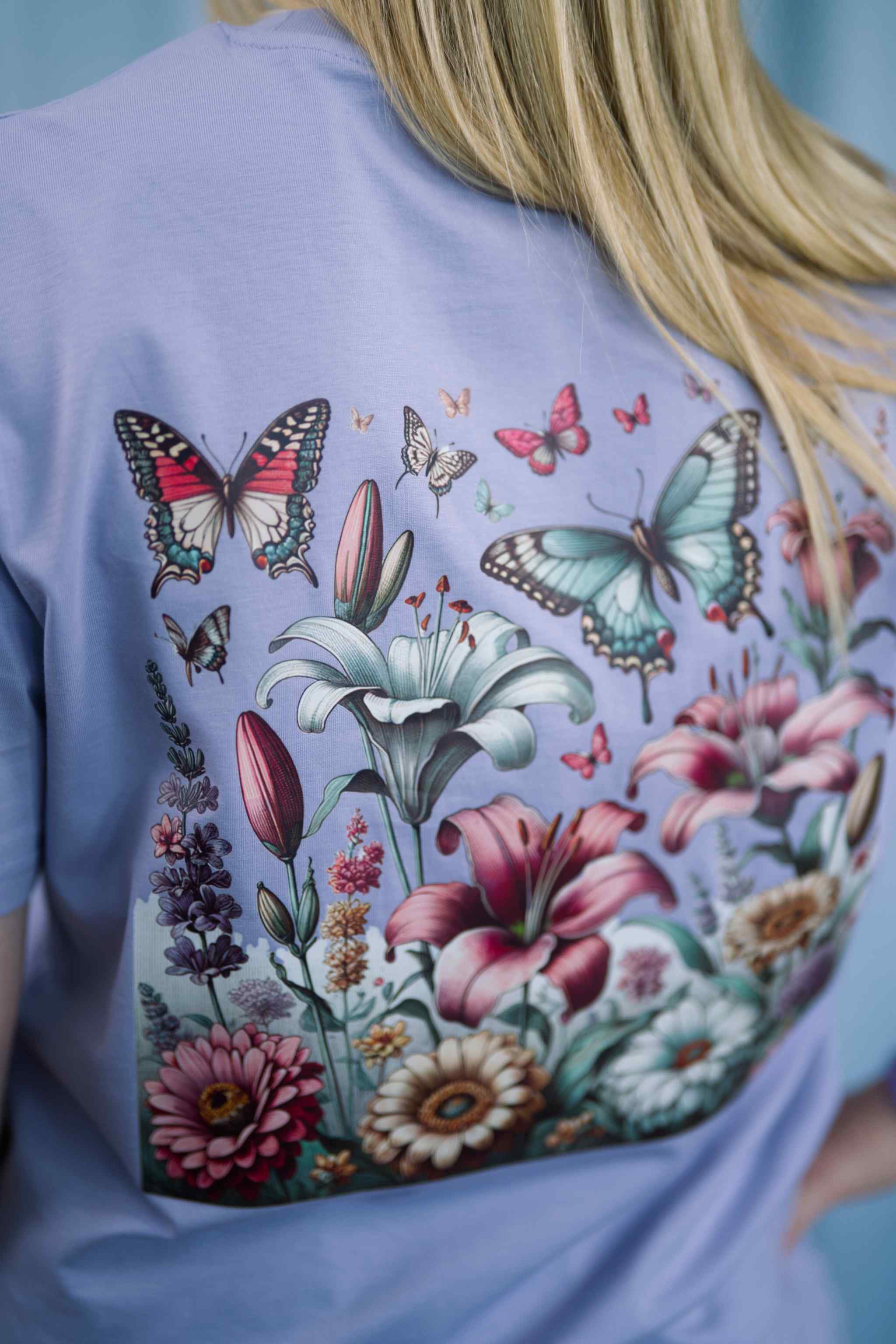 T-Shirt aus 100 % Bio-Baumwolle mit normaler Passform, erhältlich in verschiedenen Farben wie Blue Soul, Cotton Pink, Lavender, Aloe, Weiss und Schwarz. Individuell bedruckbar mit Wunschmotiv. Weiches, angenehm leichtes Material für hohen Tragekomfort. Ideal für einen zeitgemässen, entspannten Look. Vorderseite: Farbiger Schmetterling auf der linken Brust. Rückseite: Buntes Blumen- und Schmetterlingsfeld im Illustrationsstil.