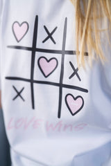 T-Shirt aus 100 % Bio-Baumwolle mit normaler Passform, erhältlich in verschiedenen Farben wie Blue Soul, Cotton Pink, Lavender, Aloe, Weiss und Schwarz. Individuell bedruckbar mit Wunschmotiv. Weiches, angenehm leichtes Material für hohen Tragekomfort. Ideal für einen zeitgemässen, entspannten Look. Tic-Tac-Toe-Motiv mit rosa Herzen und darunter der Schriftzug „LOVE WINS“ in rosa auf der Rückseite.