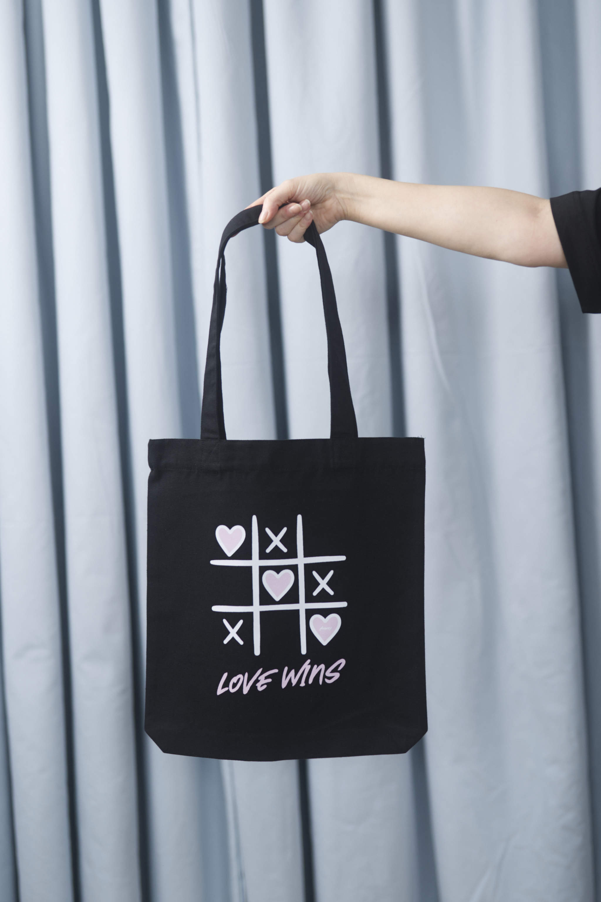 Schwarze Tote Bag mit einem verspielten Tic-Tac-Toe-Design aus weissen Linien und rosa Herzen sowie dem pinken Schriftzug „LOVE WINS“ – stilvolle Stofftasche mit Statement für Liebe und Vielfalt.