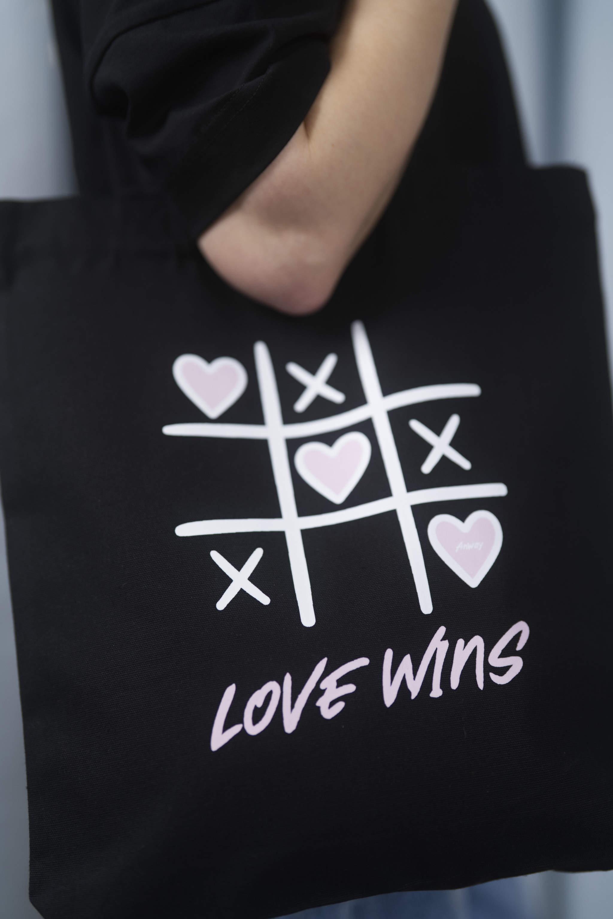 Schwarze Tote Bag mit einem verspielten Tic-Tac-Toe-Design aus weissen Linien und rosa Herzen sowie dem pinken Schriftzug „LOVE WINS“ – stilvolle Stofftasche mit Statement für Liebe und Vielfalt.