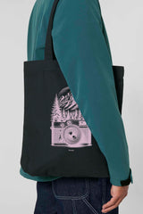 Schwarze Tote Bag mit rosa Vintage-Motiv einer analogen, alten Kamera vor einem Bergpanorama und Tannen – hochwertige Stofftasche aus 80% recycelter Baumwolle und 20% recyceltem Polyester, ideal für Natur- und Fotografie-Liebhaber.