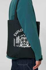 Schwarze Tote Bag mit weissem Aufdruck „EXPLORER GIRL“ – illustriert mit einem VW-Bus, Tannenbäumen und Bergen – robustes, stylisches Accessoire aus 80% recycelter Baumwolle und 20% recyceltem Polyester, fair produziert.