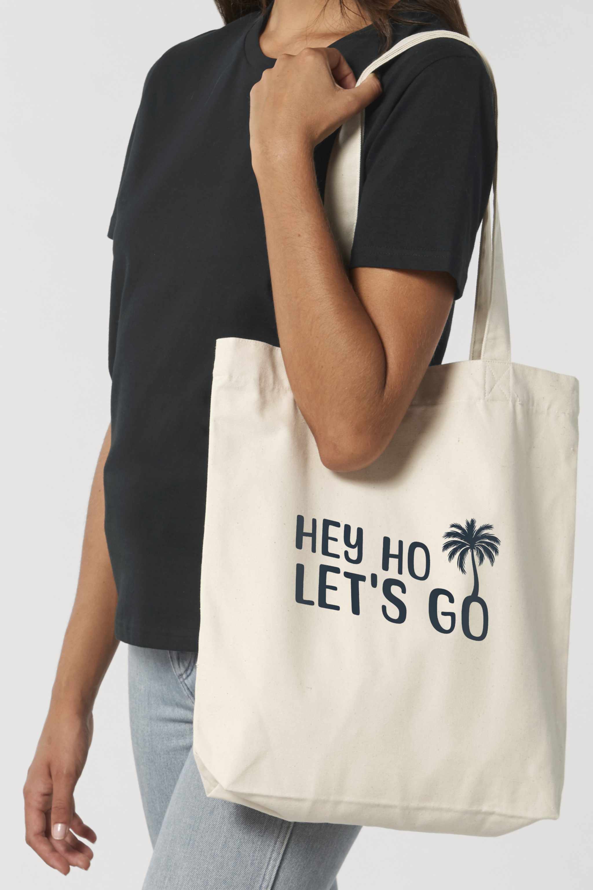 Naturfarbene Tote Bag mit schwarzem Schriftzug „HEY HO LET’S GO“ und Palmenmotiv – nachhaltige Stofftasche aus recycelten Materialien mit langen Henkeln und geräumigem Schnitt.