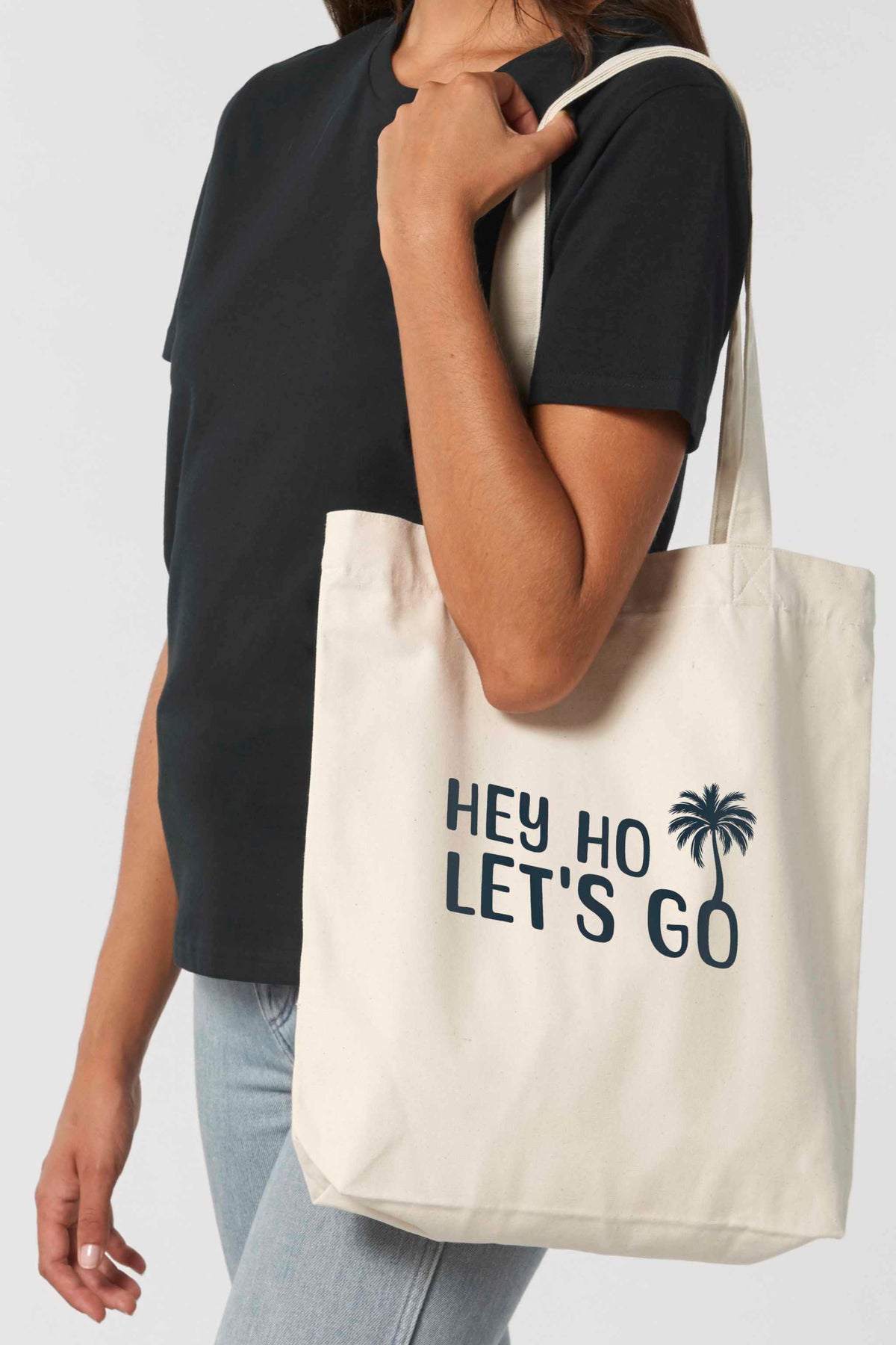 Naturfarbene Tote Bag mit schwarzem Schriftzug „HEY HO LET’S GO“ und Palmenmotiv – nachhaltige Stofftasche aus recycelten Materialien mit langen Henkeln und geräumigem Schnitt.