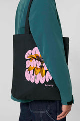Schwarze Tote Bag mit dem rosa Schriftzug „GOOD DAY TO BLOOM“ im Retro-Stil, durchzogen von einer leuchtend gelben Sonnenblume – florales Statement-Piece mit positiver Botschaft.